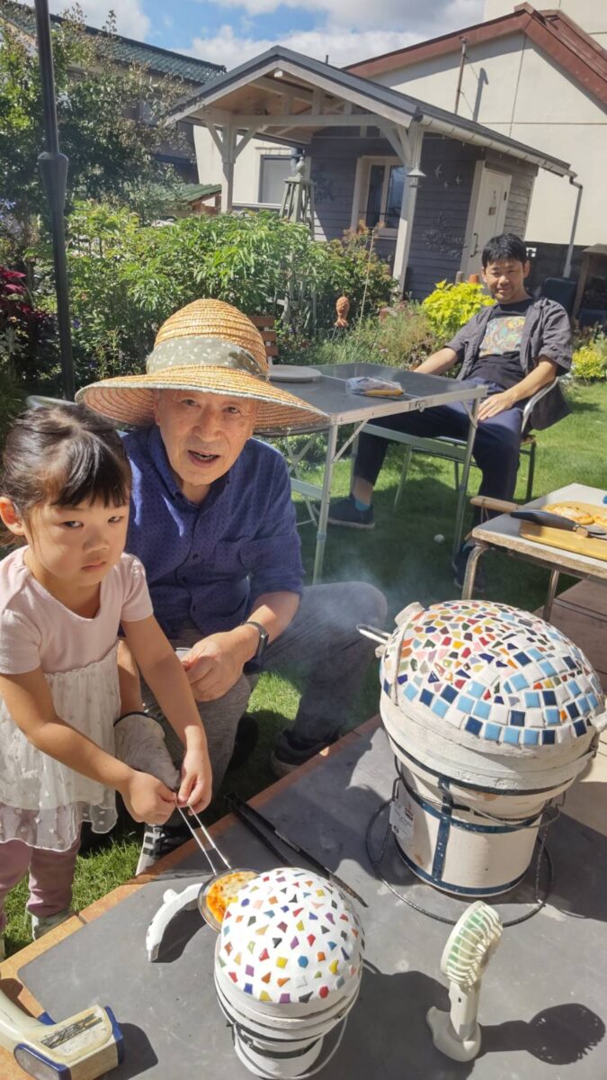 庭で石窯miniを使い、祖父とお孫さんが焼き上がったピザを取り出す様子